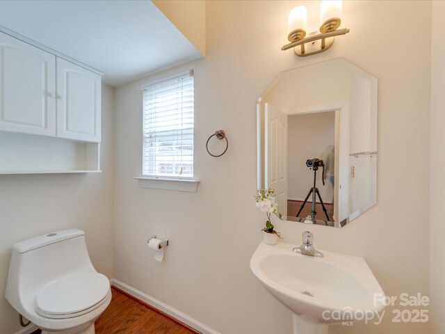 half bathroom featuring toilet, baseboards, a sink, and wood finished floors