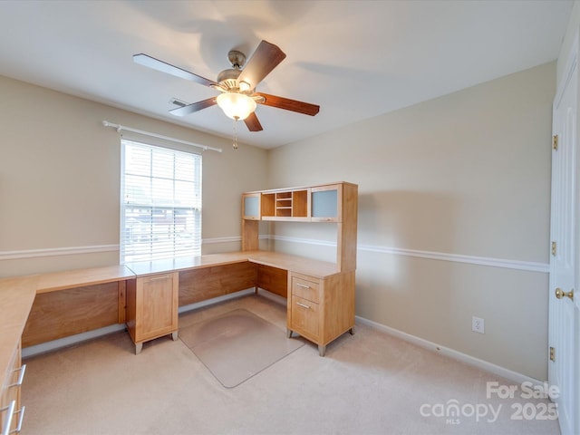 unfurnished office with baseboards, ceiling fan, built in desk, and light colored carpet