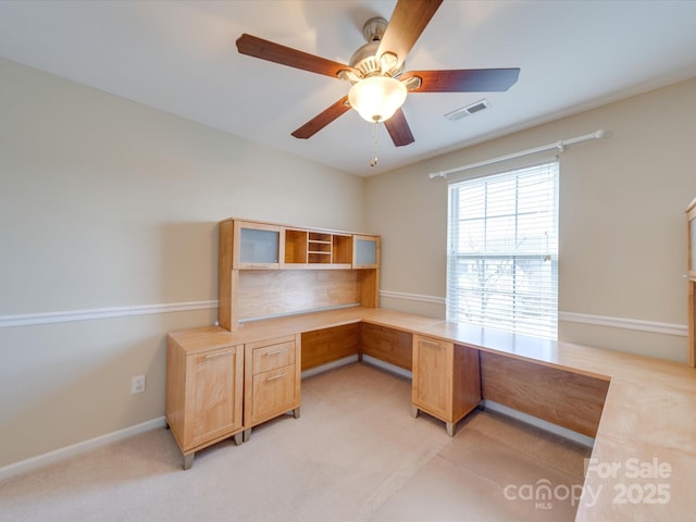 office space featuring light carpet, baseboards, visible vents, a ceiling fan, and built in study area