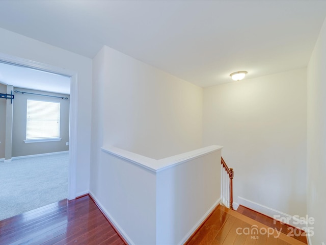 hall featuring baseboards, wood finished floors, and an upstairs landing