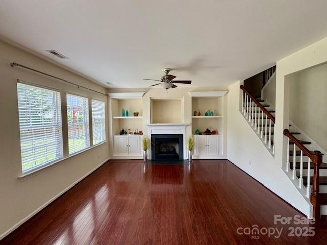 unfurnished living room featuring wood finished floors, a fireplace with flush hearth, ceiling fan, and stairs