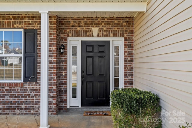 doorway to property featuring covered porch and brick siding