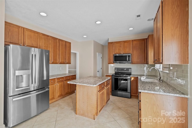 kitchen with appliances with stainless steel finishes, light tile patterned flooring, a sink, and a center island