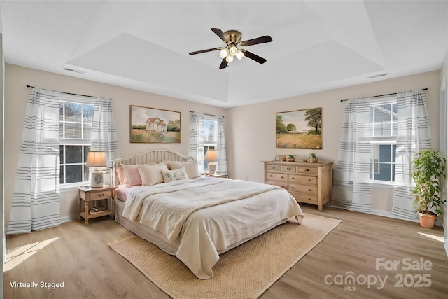 bedroom featuring visible vents, a tray ceiling, light wood-type flooring, and a ceiling fan