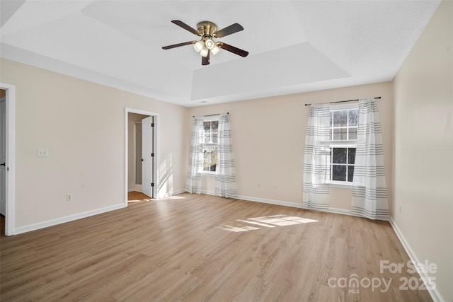 empty room featuring a tray ceiling, light wood-style flooring, and baseboards