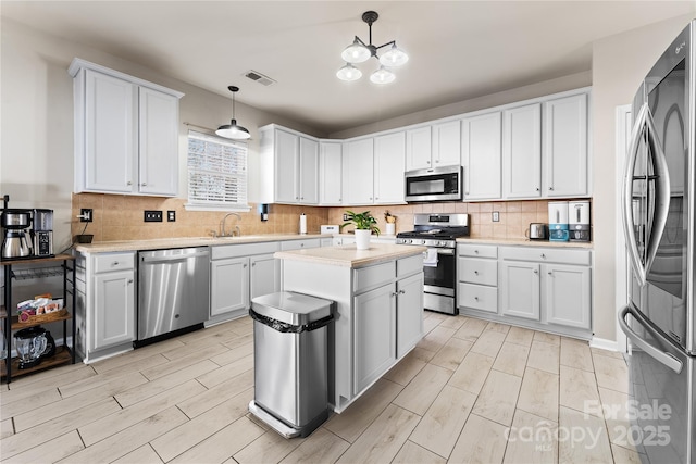 kitchen with stainless steel appliances, tasteful backsplash, light countertops, visible vents, and a sink