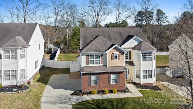 traditional home featuring driveway, fence, a front lawn, and brick siding