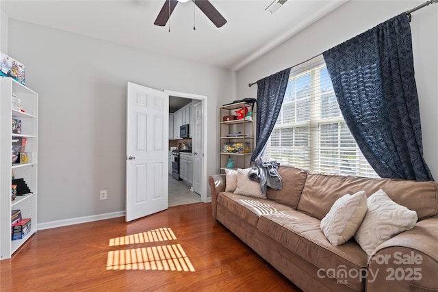 living area with visible vents, ceiling fan, baseboards, and wood finished floors