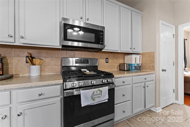 kitchen with light wood finished floors, stainless steel appliances, decorative backsplash, white cabinetry, and light stone countertops