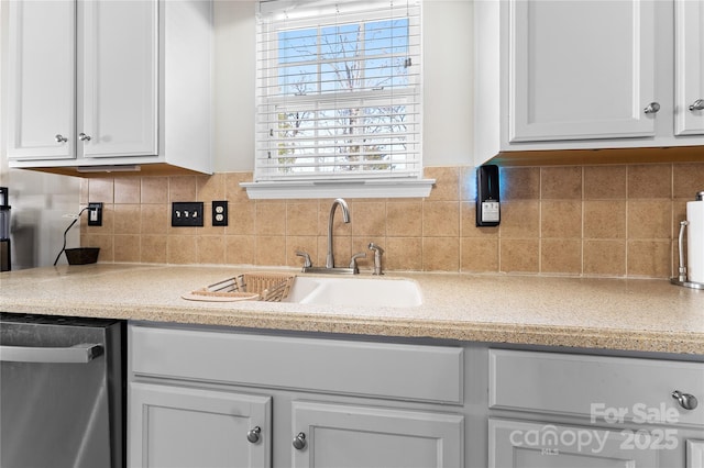 kitchen featuring dishwasher, backsplash, a sink, and white cabinetry