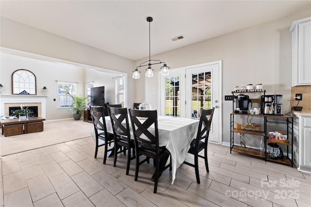 dining area featuring light colored carpet, a fireplace, visible vents, baseboards, and wood tiled floor