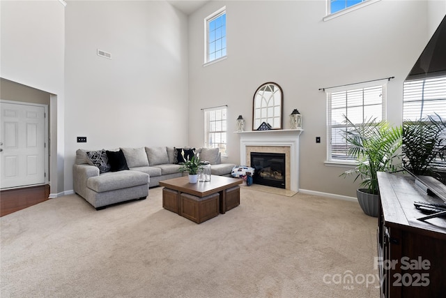 living area featuring a glass covered fireplace, light colored carpet, visible vents, and baseboards