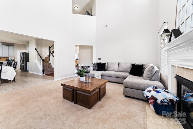 living area featuring light colored carpet, a towering ceiling, baseboards, stairs, and a glass covered fireplace