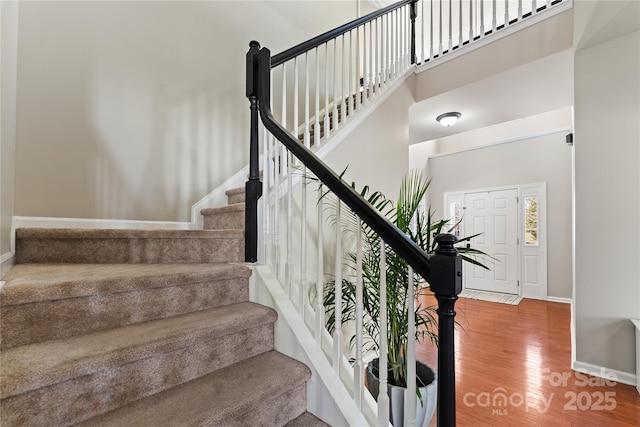 stairs featuring a towering ceiling, baseboards, and wood finished floors