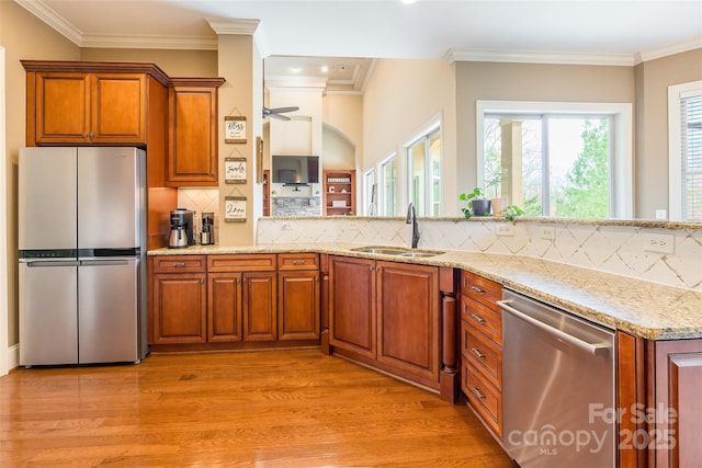 kitchen featuring brown cabinetry, light stone counters, stainless steel appliances, light wood-type flooring, and a sink