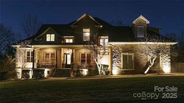 view of front of property featuring a porch, stone siding, and a lawn