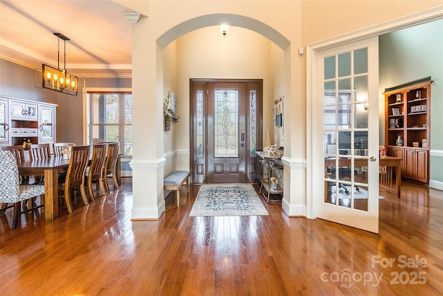 entrance foyer featuring baseboards, arched walkways, hardwood / wood-style flooring, ornamental molding, and a chandelier