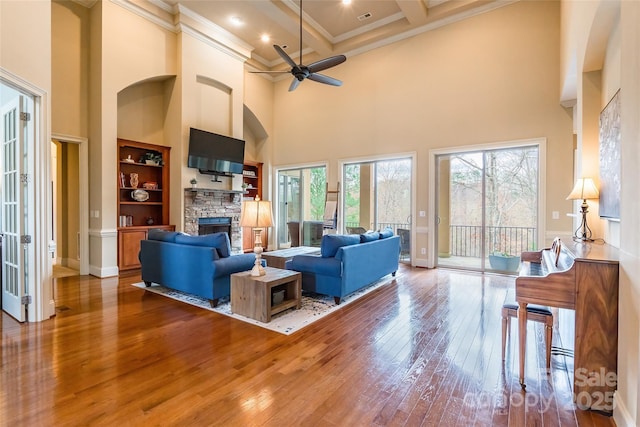 living area with built in features, wood-type flooring, ornamental molding, beamed ceiling, and a fireplace