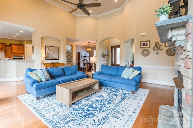 living area with arched walkways, ceiling fan, a fireplace, ornamental molding, and light wood finished floors