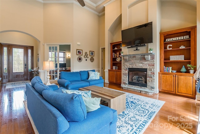 living room featuring a high ceiling, a fireplace, light wood-style flooring, and crown molding