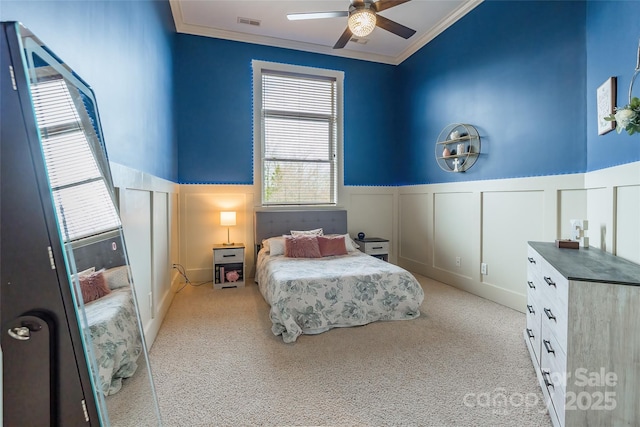 bedroom with light carpet, a ceiling fan, visible vents, wainscoting, and crown molding