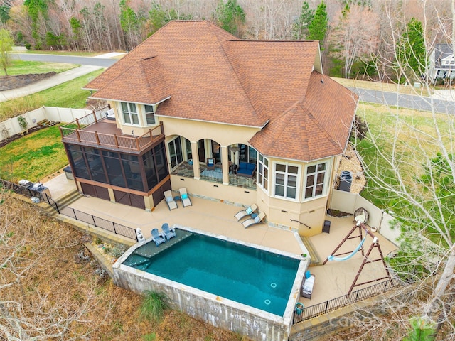 back of property with roof with shingles, stucco siding, a sunroom, a patio area, and a fenced backyard