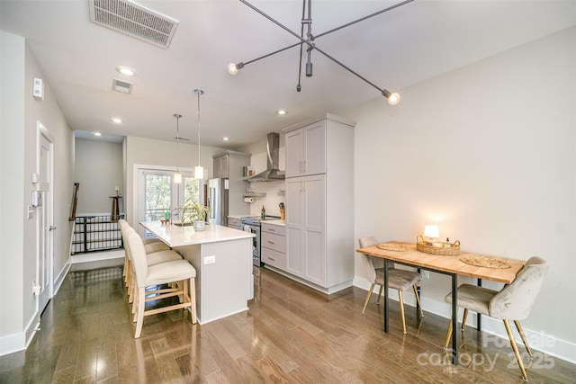 kitchen featuring visible vents, a center island with sink, stainless steel electric range oven, wall chimney exhaust hood, and dark wood-style flooring