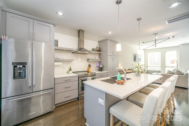 kitchen with visible vents, open shelves, a sink, appliances with stainless steel finishes, and wall chimney range hood