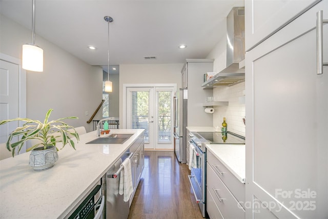 kitchen featuring a sink, backsplash, dark wood finished floors, stainless steel appliances, and wall chimney range hood