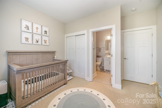 bedroom featuring ensuite bath, baseboards, a closet, and light carpet