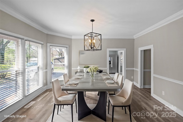 dining area with baseboards, visible vents, wood finished floors, crown molding, and a notable chandelier