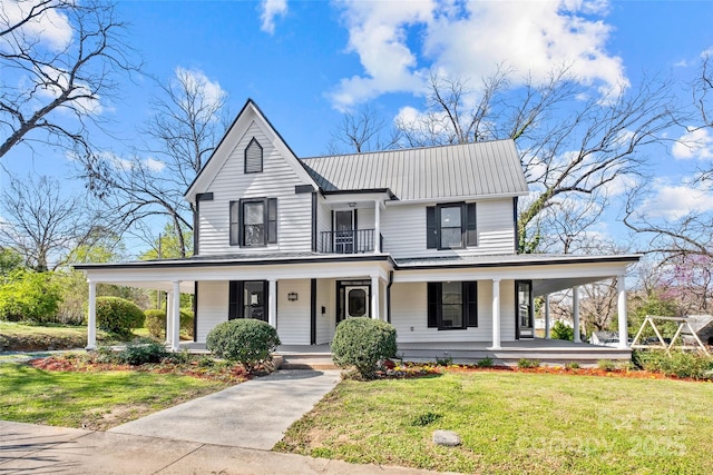 country-style home with covered porch, metal roof, a front yard, and a balcony