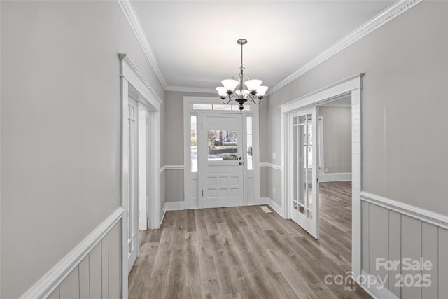 foyer featuring light wood-type flooring, a chandelier, crown molding, and wainscoting