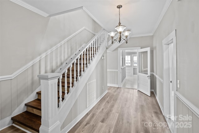 staircase featuring a chandelier, a decorative wall, wood finished floors, visible vents, and crown molding