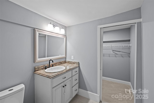 bathroom with toilet, baseboards, a walk in closet, and vanity