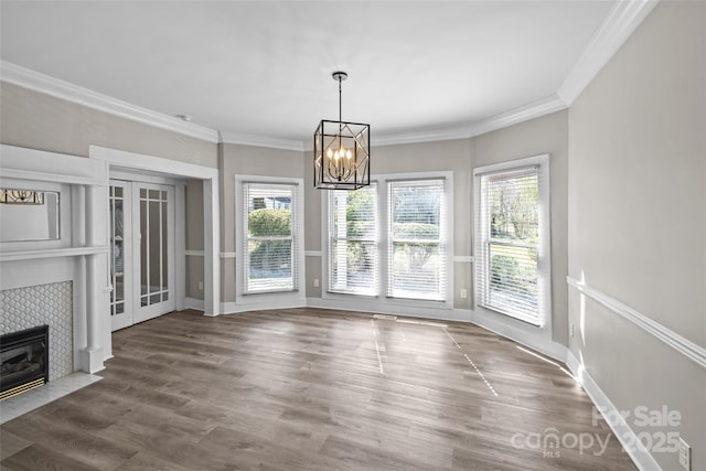 unfurnished dining area with a tile fireplace, crown molding, wood finished floors, baseboards, and an inviting chandelier