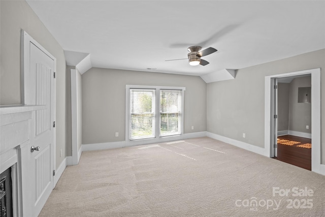 interior space featuring vaulted ceiling, light carpet, a fireplace, and baseboards