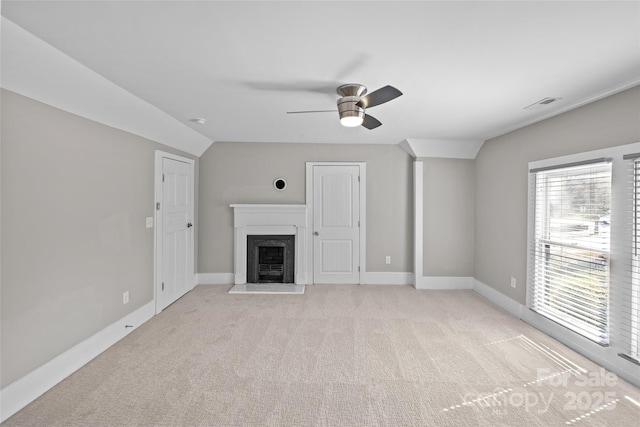 unfurnished living room featuring light colored carpet, visible vents, a fireplace with flush hearth, vaulted ceiling, and baseboards