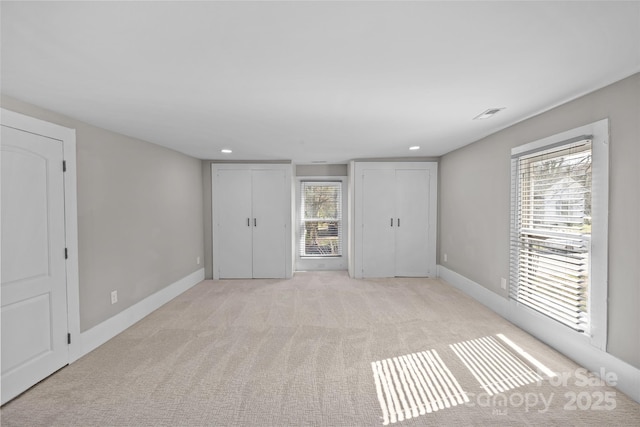 unfurnished bedroom featuring multiple closets, recessed lighting, light colored carpet, and baseboards