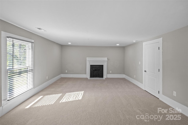 unfurnished living room with light carpet, visible vents, baseboards, a fireplace with flush hearth, and recessed lighting