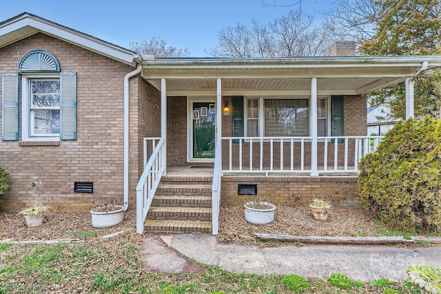 view of front of home with a porch, crawl space, a chimney, and brick siding