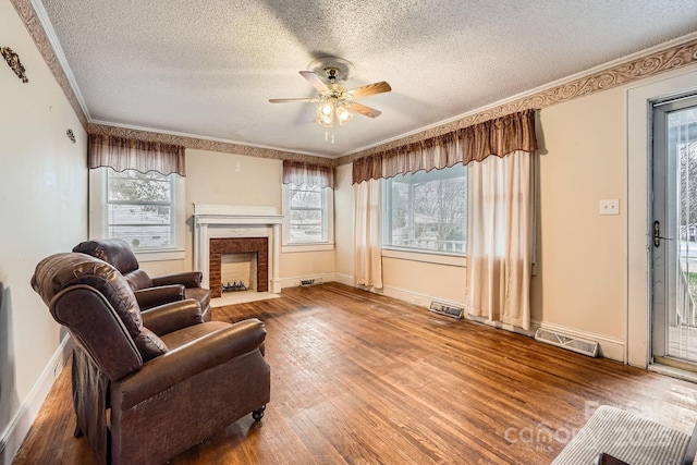 living area with visible vents, baseboards, wood-type flooring, ceiling fan, and ornamental molding