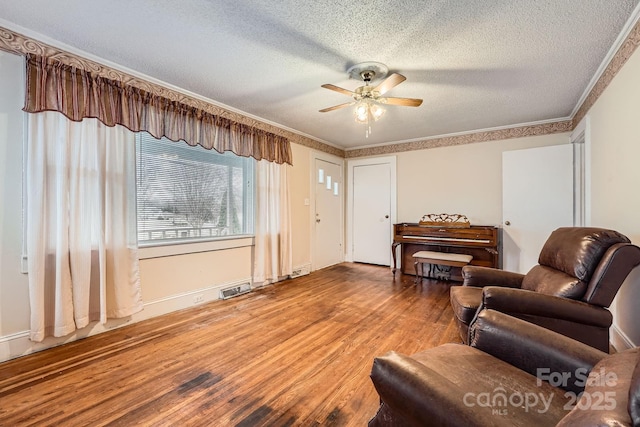 living room with a textured ceiling, ceiling fan, wood finished floors, and crown molding