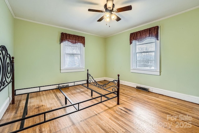 bedroom featuring a baseboard radiator, visible vents, ornamental molding, baseboards, and hardwood / wood-style flooring