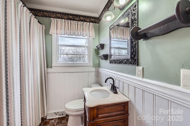 bathroom featuring brick floor, a wainscoted wall, crown molding, toilet, and vanity