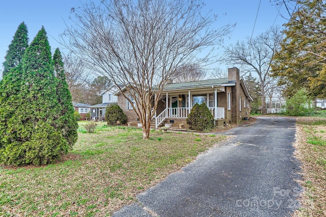 view of front of home featuring aphalt driveway, brick siding, a chimney, covered porch, and crawl space