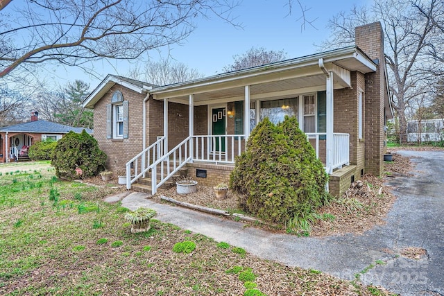 bungalow-style home featuring covered porch, brick siding, a chimney, and aphalt driveway