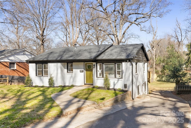 single story home featuring a front yard, brick siding, fence, and roof with shingles