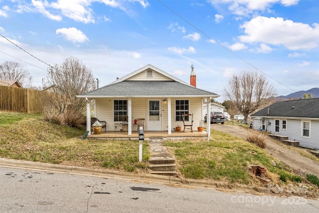 bungalow-style house featuring a porch, a shingled roof, a chimney, and fence