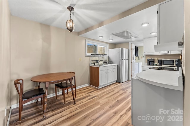 kitchen featuring baseboards, light countertops, light wood-style flooring, appliances with stainless steel finishes, and a sink